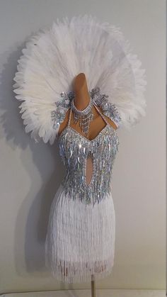 a mannequin with white feathers and chains on it's back, in front of a wall