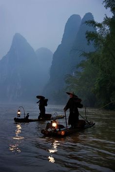 two people on small boats in the water with mountains in the backgrouds