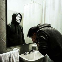 a man in a black hoodie is looking at his face in the bathroom mirror