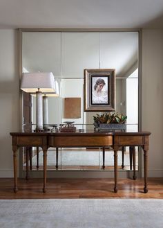 a large mirror sitting on top of a wooden table next to a lamp and vase