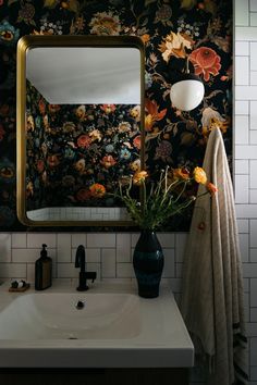 a bathroom sink sitting under a mirror next to a vase with flowers on top of it