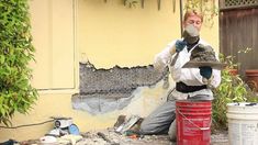 a man sitting on the ground next to a red trash can with a mask covering his face