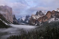 the mountains are covered in snow and fog as they sit on top of a mountain