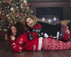 two women laying on the floor in matching christmas sweaters and ugly hair, smiling at the camera