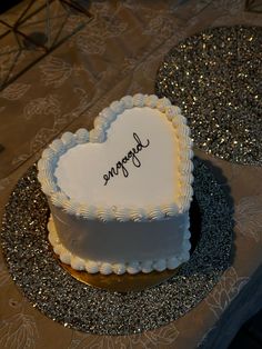 a heart shaped cake on a table with silver glitters and a name written on it