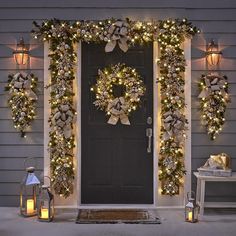 christmas wreaths and lights decorate the front door of a house with two lanterns on either side