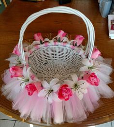 a white basket with pink flowers and tulle sitting on top of a wooden table