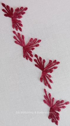 red embroidered flowers on white fabric with stitching in the center and two leaves at the bottom