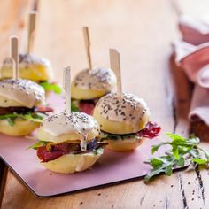 four mini sandwiches with toppings on a pink plate next to a napkin and fork