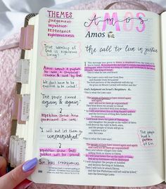 a hand holding an open bible with pink writing on the pages and some other words