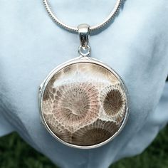 Introducing our exquisite Sterling Silver Petoskey Stone Locket Pendant, a perfect blend of beauty and elegance! This stunning locket features a genuine 23mm diameter Petoskey Stone set in high-quality Sterling Silver. The captivating fossilized coral, known as hexagonaria, dates back approximately 350 million years to the Devonian era, making it a true piece of ancient history. Wear this unique pendant close to your heart and embrace the essence of Michigan's geological heritage. The Petoskey Stone is a treasured symbol of the state, found along the scenic shores of Lake Michigan and Lake Huron. The locket's craftsmanship showcases the natural beauty of the stone, making it a timeless addition to your jewelry collection. Whether as a gift or a personal keepsake, this locket will surely be Petoskey Stone, Fossilized Coral, Lake Huron, Unique Pendant, Lake Michigan, Ancient History, Stone Settings, Sterling Silber, Devon