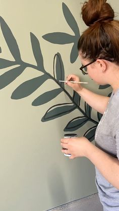 a woman painting a wall with leaves on it