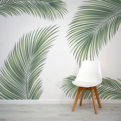 a white chair sitting in front of a palm leaf wallpaper