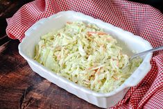 a white dish filled with coleslaw on top of a red and white checkered cloth