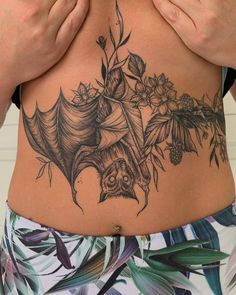 a woman with a bat tattoo on her stomach and flowers around her waist, holding her hands to her chest