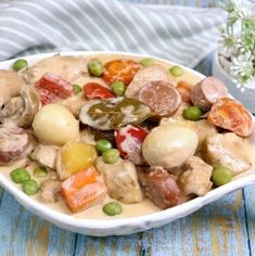 a white bowl filled with meat and vegetables on top of a blue wooden table next to a potted plant