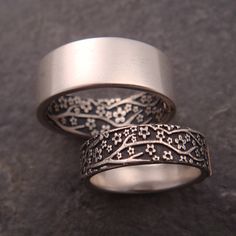 two silver rings with intricate designs on them sitting on a stone surface in front of a black background