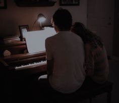 two people sitting at a piano in the dark