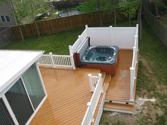 a hot tub sitting on top of a wooden deck next to a fence and green grass