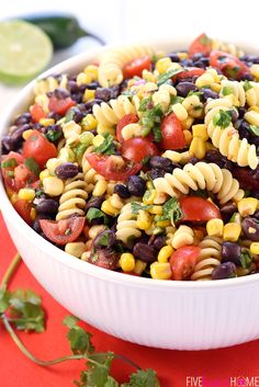 a white bowl filled with pasta salad on top of a red cloth next to cilantro