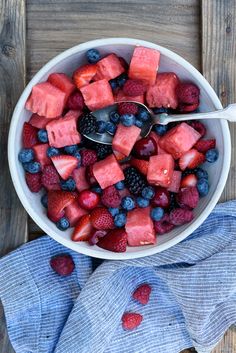 a bowl filled with watermelon, blueberries and raspberries on top of a wooden table