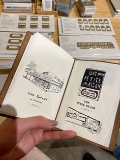 a person holding an open book in front of some other books on a counter top