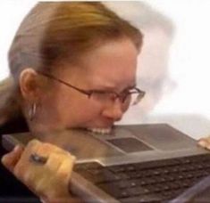 a woman with glasses is biting into a laptop