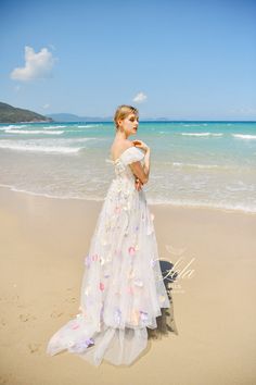 a woman standing on top of a beach next to the ocean wearing a white dress