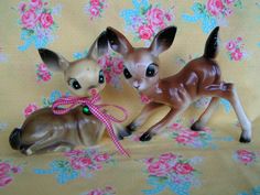 two small deer figurines sitting on top of a floral covered bed sheet next to each other