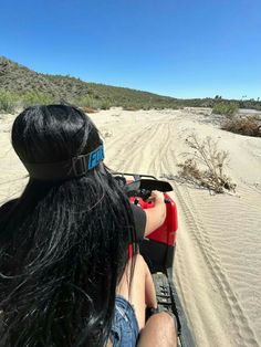 a woman riding on the back of a red four - wheeler down a sandy road