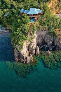 an aerial view of a house on top of a cliff next to the ocean with clear blue water