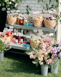 an outdoor fruit and vegetable stand with flowers in buckets on the grass, labeled with labels