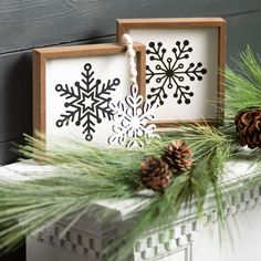 two snowflakes and pine cones are sitting on a mantle