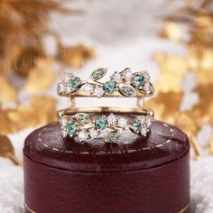 two gold rings with green and white stones on top of a wooden box in front of snow