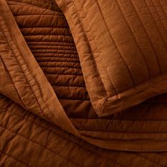 an orange quilted comforter and pillow on top of a brown bed coverlet