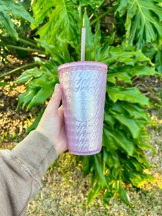 a person is holding a pink cup with a straw in front of some bushes and trees