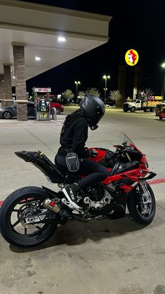 a person on a red motorcycle parked in a parking lot with gas pumps behind them