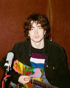 a young man sitting in front of a microphone holding a guitar