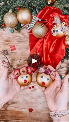 two hands holding christmas ornaments in front of a wooden table with red and gold decorations