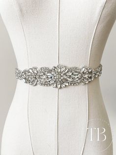 "Crafted from dazzling rhinestones, this exquisite sash exudes elegance. The rhinestone segment measures 11.5\" inches long and about 1.75\" wide at the widest point. Ribbon Constructed with satin or organza ribbon, the choice is yours, measuring 31 inches in length on each side. An opulent and stylish bridal belt." Silver Fitted Bridal Belt, Fitted Silver Bridal Belt For Bride, Fitted Bridal Belt With Rhinestones And Crystal, Bridal Belt With Rhinestones And Crystal, Formal Crystal Sash With Rhinestones, Crystal Bridal Belt With Rhinestones For Wedding, Formal Crystal Sashes With Rhinestones, Formal Crystal Rhinestone Sash, Silver Rhinestone Bridal Belt For Prom