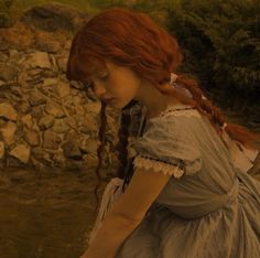 a woman with red hair is standing in front of a stone wall and looking down