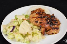 a white plate topped with chicken and rice next to a salad on a black table