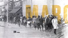 a group of people walking down a street next to a tall yellow sign that says marq