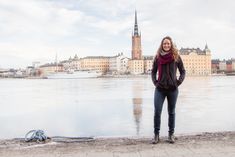 a woman standing in front of a body of water with buildings behind her and a snake laying on the ground