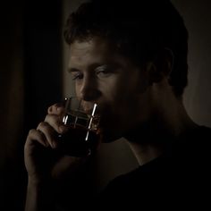 a young man drinking from a glass in the dark with his hand on his mouth