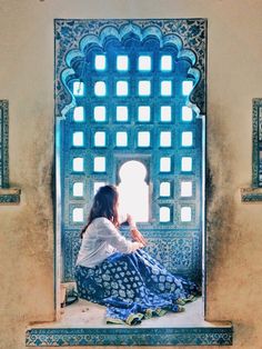 a woman sitting on top of a window sill in front of a blue and white wall