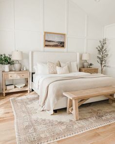 a bedroom with white walls and wood flooring has a bed, two nightstands, and a bench