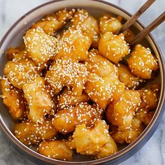 a bowl filled with fried chicken and sesame seeds next to chopsticks on a table