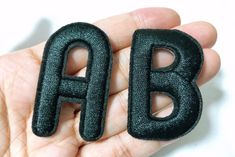 a person holding two small black letters in their hand, the letter b is made out of leather