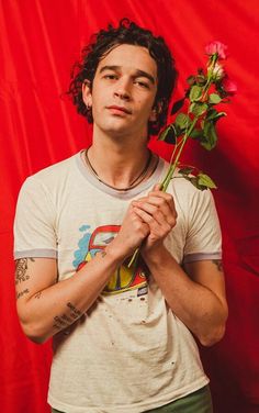 a young man is holding a rose in front of his face while standing against a red background